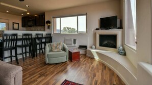 A living room with a fireplace, a dining area with chairs, a television, and a ceiling fan. - Moab Indian Hills - Secluded Breathtaking Views (Moab)