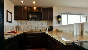 A kitchen with dark wooden cabinets, a tiled backsplash, granite countertops, a microwave, and a window with a wreath. - Moab Indian Hills - Secluded Breathtaking Views (Moab)