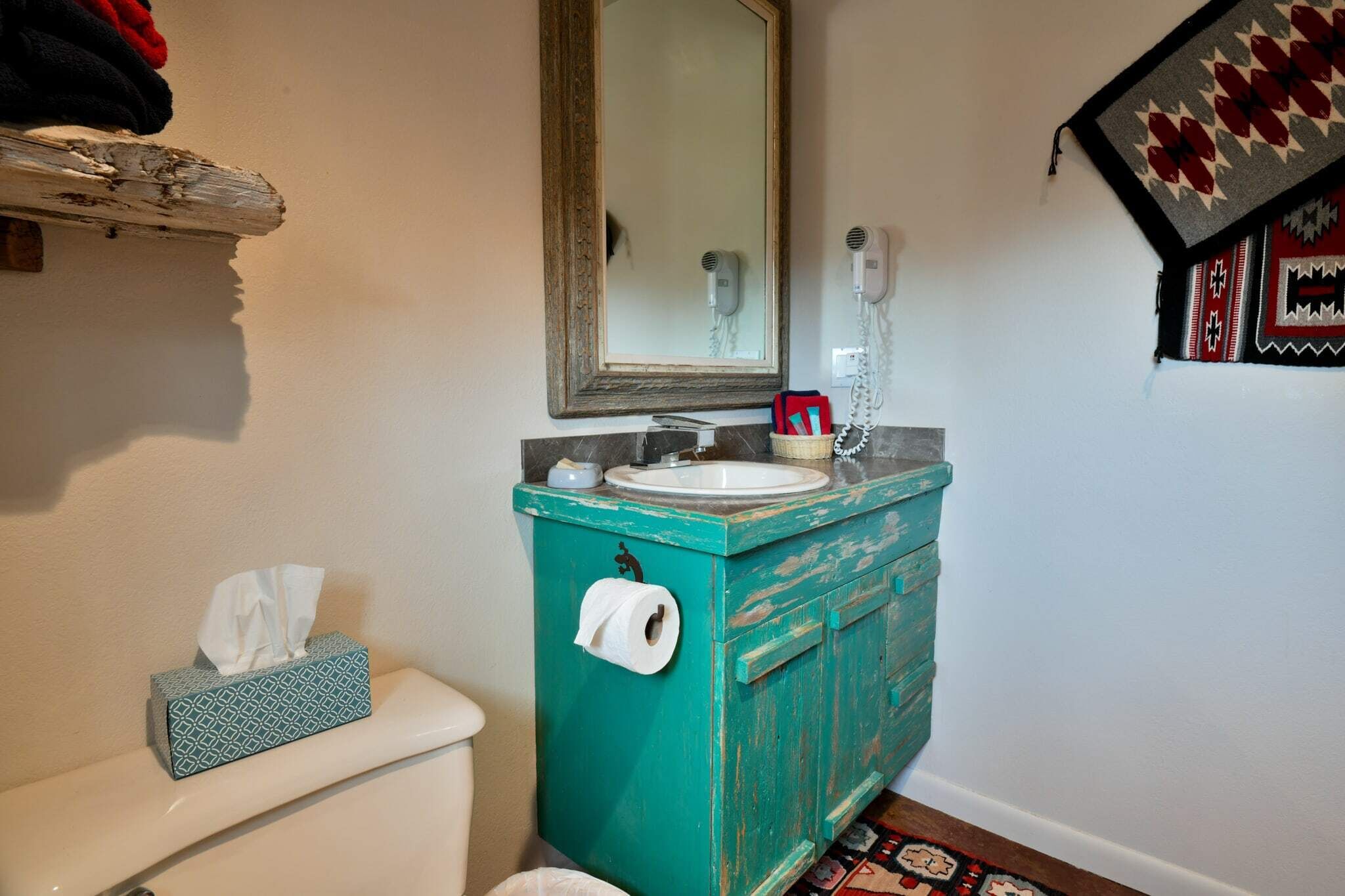 Ein Badezimmer mit einer weißen Toilette, einem türkisblauen Schrank mit Spiegel darüber und einem gemusterten Teppich auf dem Boden.