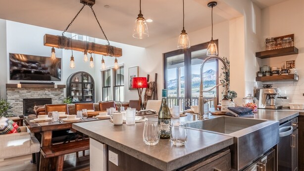 A modern kitchen with a large island, pendant lighting, and a view of mountains through the window.