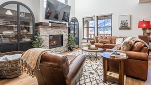 A spacious living room with a stone fireplace, leather furniture, and large windows offering mountain views.