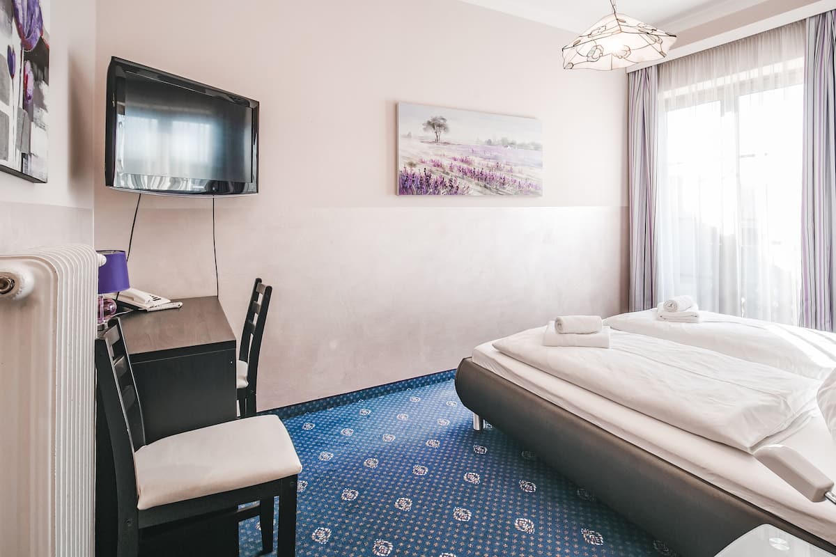 Habitación de hotel con cama, escritorio con silla, televisor montado en la pared y un cuadro.