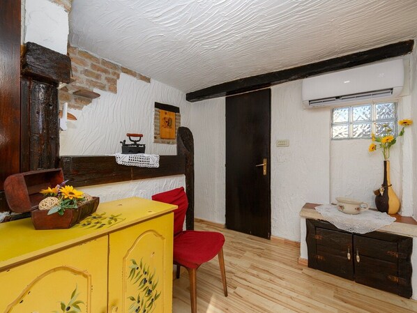 A room with a wooden floor, a yellow cabinet, a red chair, a black door, and a window with a vase of flowers.