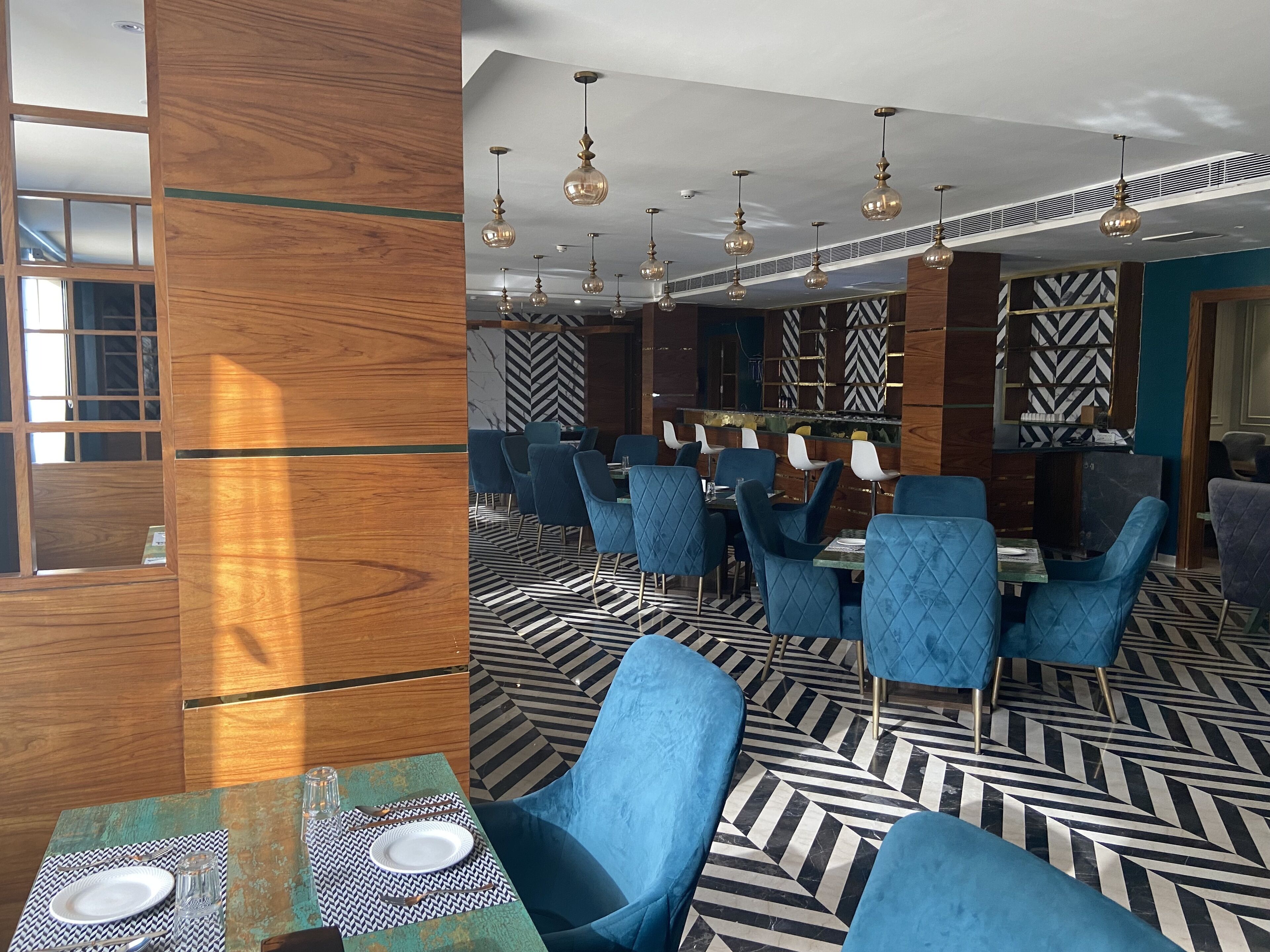 Un restaurante moderno con sillas tapizadas en azul, piso con estampado blanco y negro y lámparas esféricas colgantes.