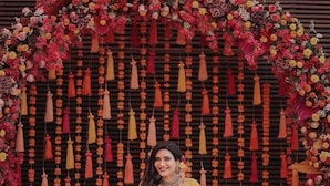 Una mujer sentada en un sofá frente a un fondo floral y adornos colgantes.