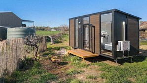 A modern, compact cabin with a large glass door, a small wooden deck, and an air conditioning unit.