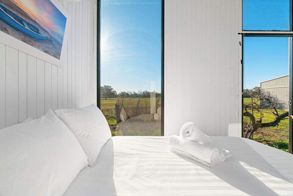 Ein Schlafzimmer mit großem Fenster, einem Bett mit weißer Bettwäsche und einem Gemälde an der Wand.