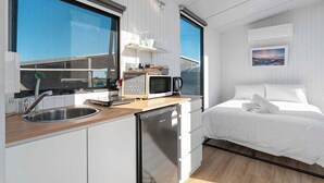 A compact room with a kitchenette, a bed, a small refrigerator, and a window with a view.