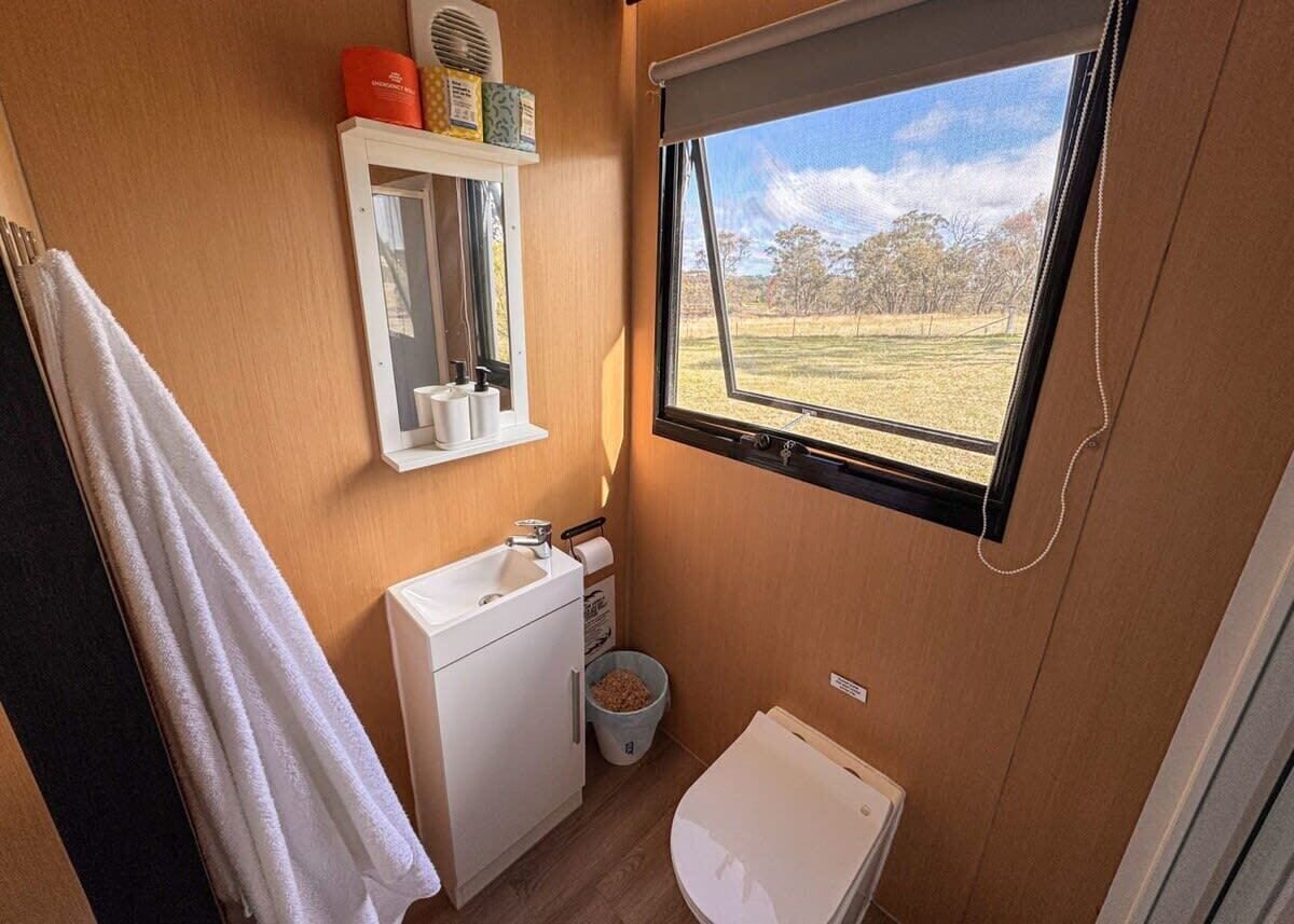 A compact bathroom with a window, a sink, a mirror, and a toilet.