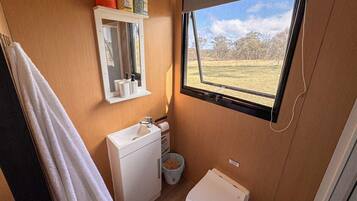 A compact bathroom with a window, a sink, a mirror, and a toilet.