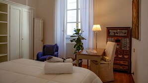 Une chambre à coucher comprenant un lit, une chaise, une table, un radiateur, une fenêtre avec des rideaux et un meuble fixé au mur.