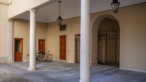 Une cour intérieure abritée par des colonnes, un vélo et une entrée fermée par un portail.