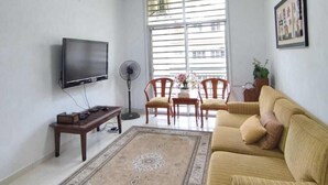 A living room with a sofa, TV, fan, and a dining area with chairs and a table.