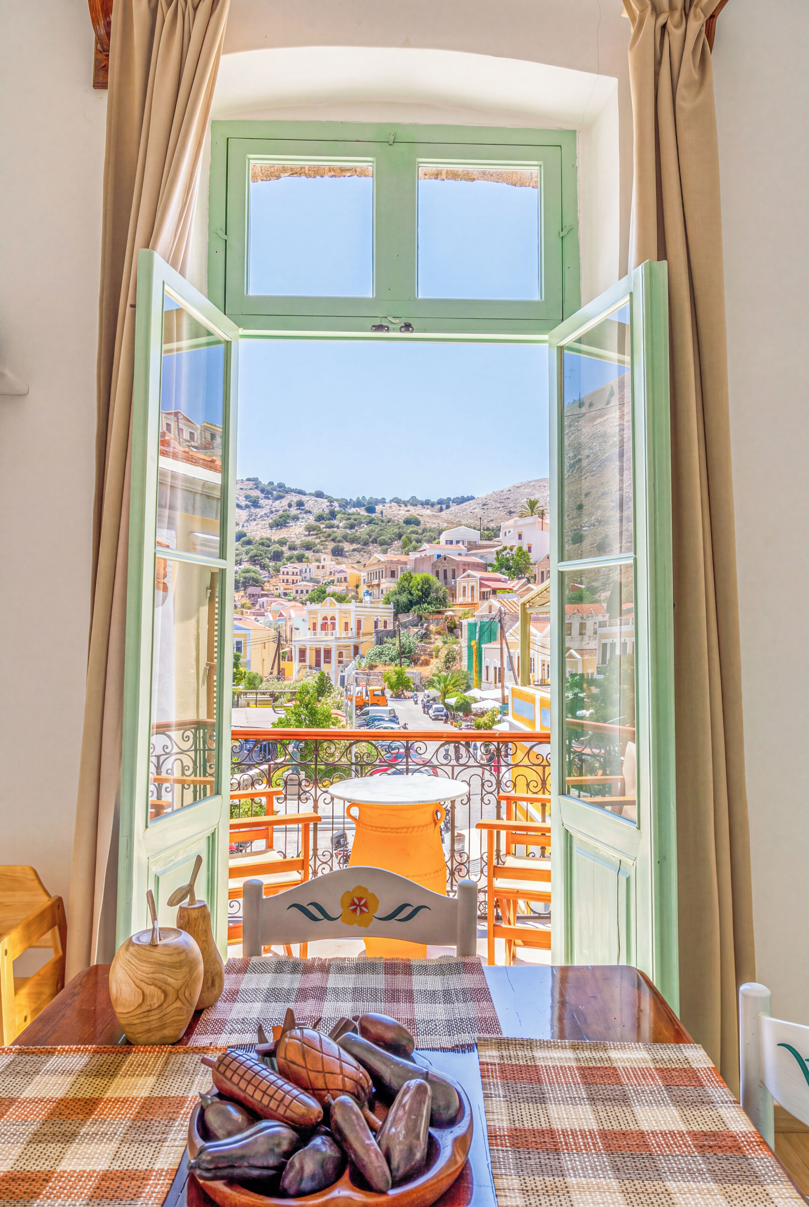 Una habitación con vistas a un pueblo a través de una ventana abierta, una mesa con un mantel individual y una silla.