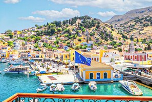 A coastal town with colorful buildings, a marina with boats, and a hill with vegetation. - Athenas - Neoclassic Harbour View (Symi)