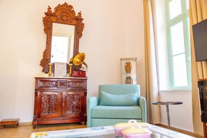 Una habitación con un armario de madera, un sillón azul, una mesita y un espejo.