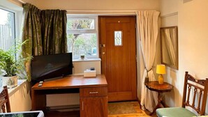 A compact room with a wooden desk, a television, a small table with a lamp, a chair, and a door with a window. - Fab Studio Room in Botley, Oxford (Oxford)