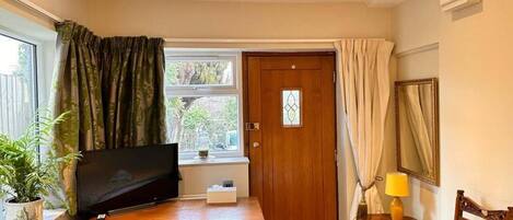 A compact room with a wooden desk, a television, a small table with a lamp, a chair, and a door with a window.