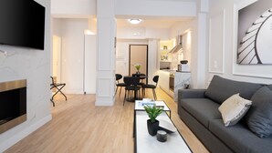 A modern living room with a flat-screen TV, a fireplace, a grey sofa, and a dining area with a table and chairs.