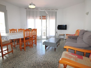 A dining area with a table and chairs, a sofa, a television, and a window with curtains.
