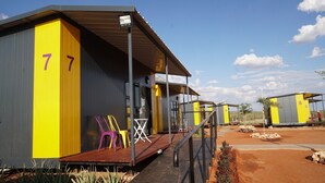 A row of numbered cabins with a covered porch and outdoor seating. - SleepOver Upington (Upington)