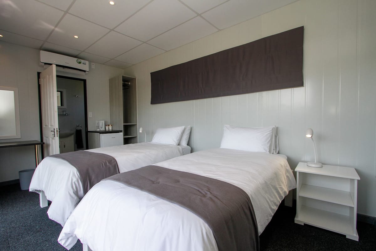 Une chambre d’hôtel avec deux lits, un bureau, une chaise, une petite table, une lampe et un climatiseur fixé au mur.