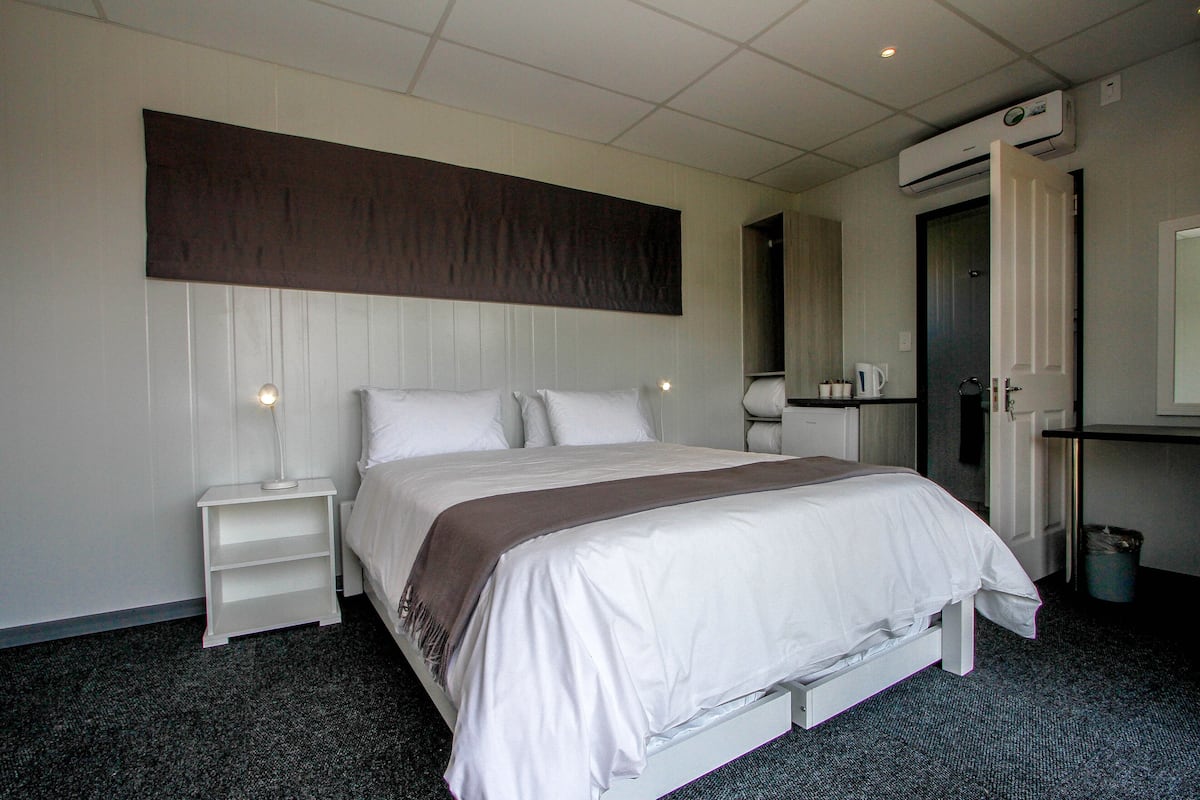 Une chambre d’hôtel comprenant un lit, une table de chevet, une commode, une armoire et un appareil de climatisation.
