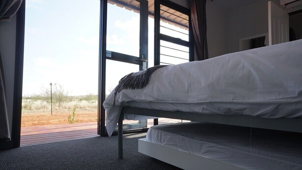 A bed in a room with large windows, a view of the desert landscape, and a modern design. - SleepOver Upington (Upington)