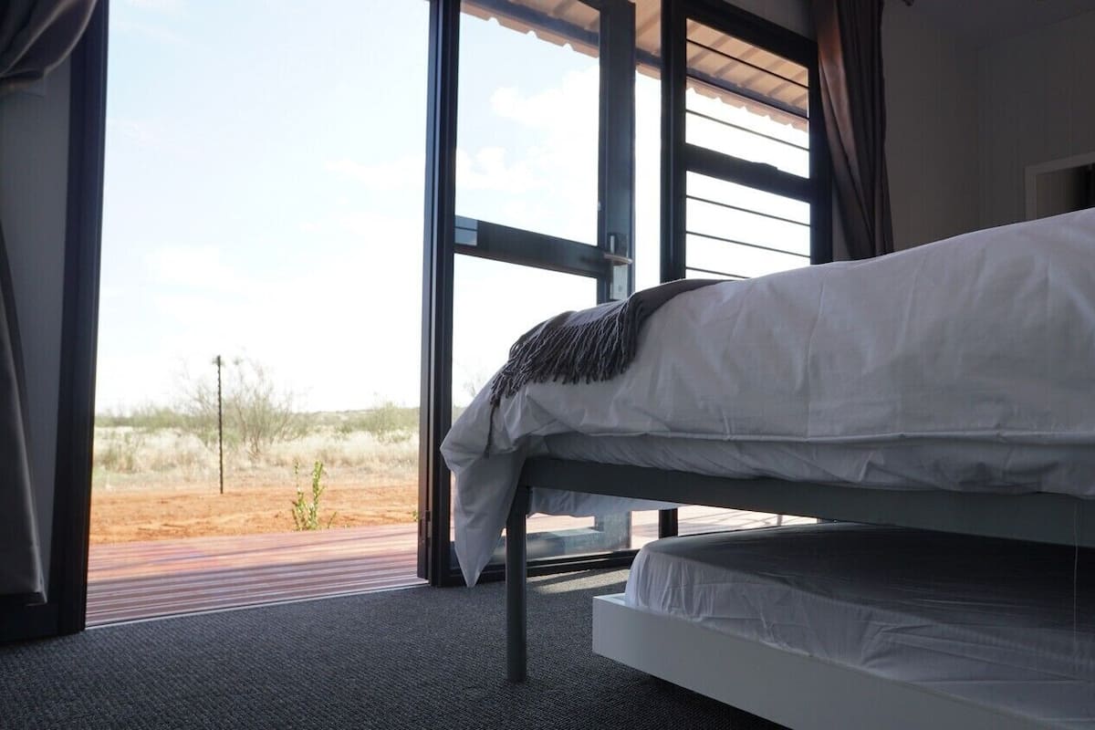Un lit dans une chambre dotée de grandes fenêtres, offrant une vue sur le paysage désertique, et présentant un design moderne.