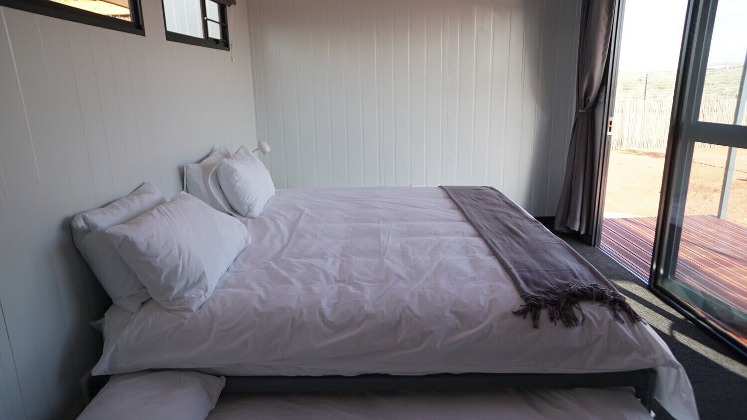 A bed with white bedding, a dark throw blanket, and a window with curtains.