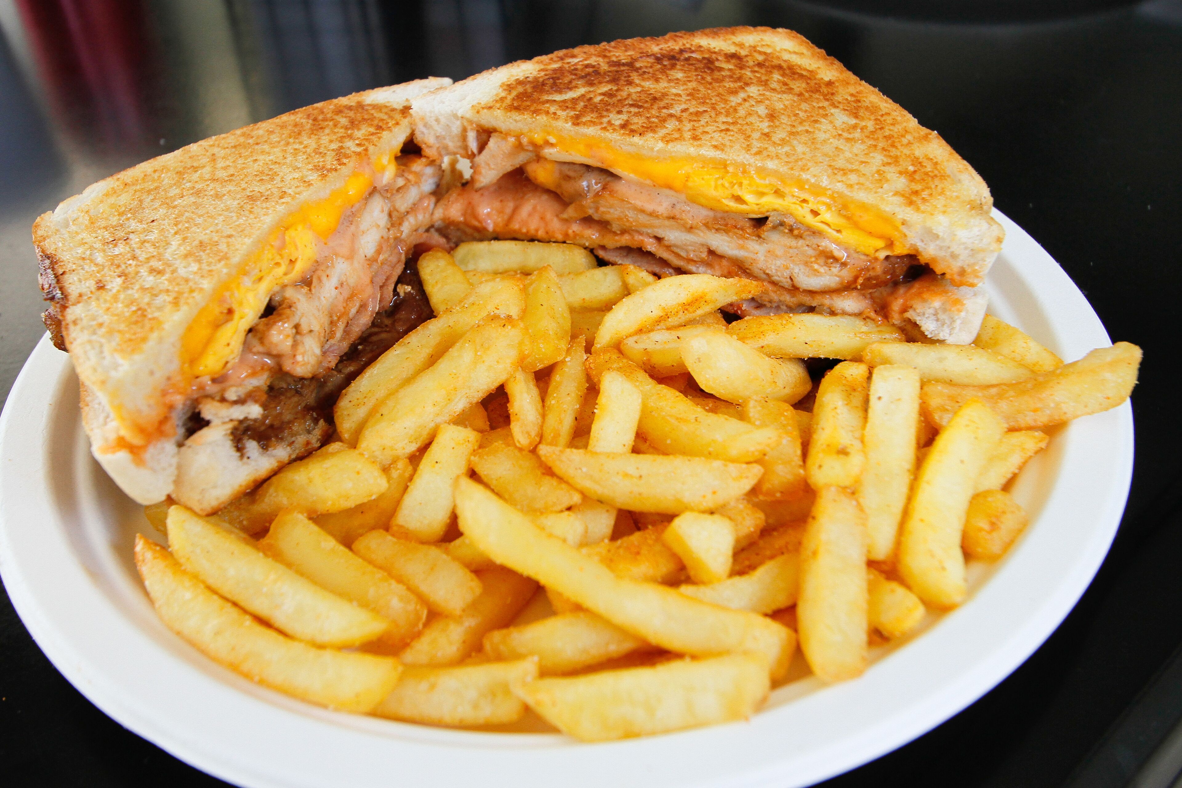 A grilled sandwich cut in half with melted cheese and meat, served with a side of French fries.