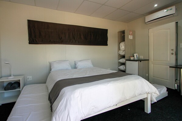 A hotel room with a bed, a bedside table with a lamp, a wardrobe, and a large artwork on the wall. - SleepOver Upington (Upington)