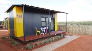 A single-room structure with a number '16' on its side, a small porch with two chairs, and a door with a window. - SleepOver Upington (Upington)