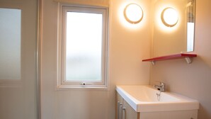 Ein Badezimmer mit einem weißen Waschbecken, einem Spiegel und einem Milchglasfenster.