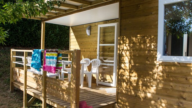 Eine Holzterrasse mit einer Bank und einem Tisch, eine Tür zum Innenbereich und ein Fenster.