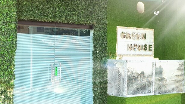 Persiana fechada com placa 'GREEN HOUSE', parede verde e cerca branca.