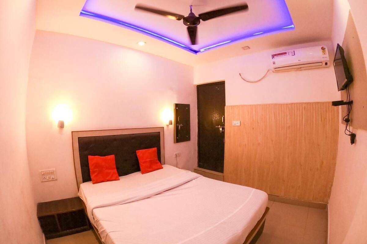 Une chambre à coucher comprenant un lit, un ventilateur de plafond, un appareil de climatisation et un téléviseur fixé au mur.