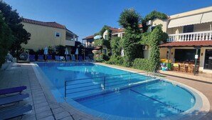 Una piscina con sillones de descanso y zona de restaurante.