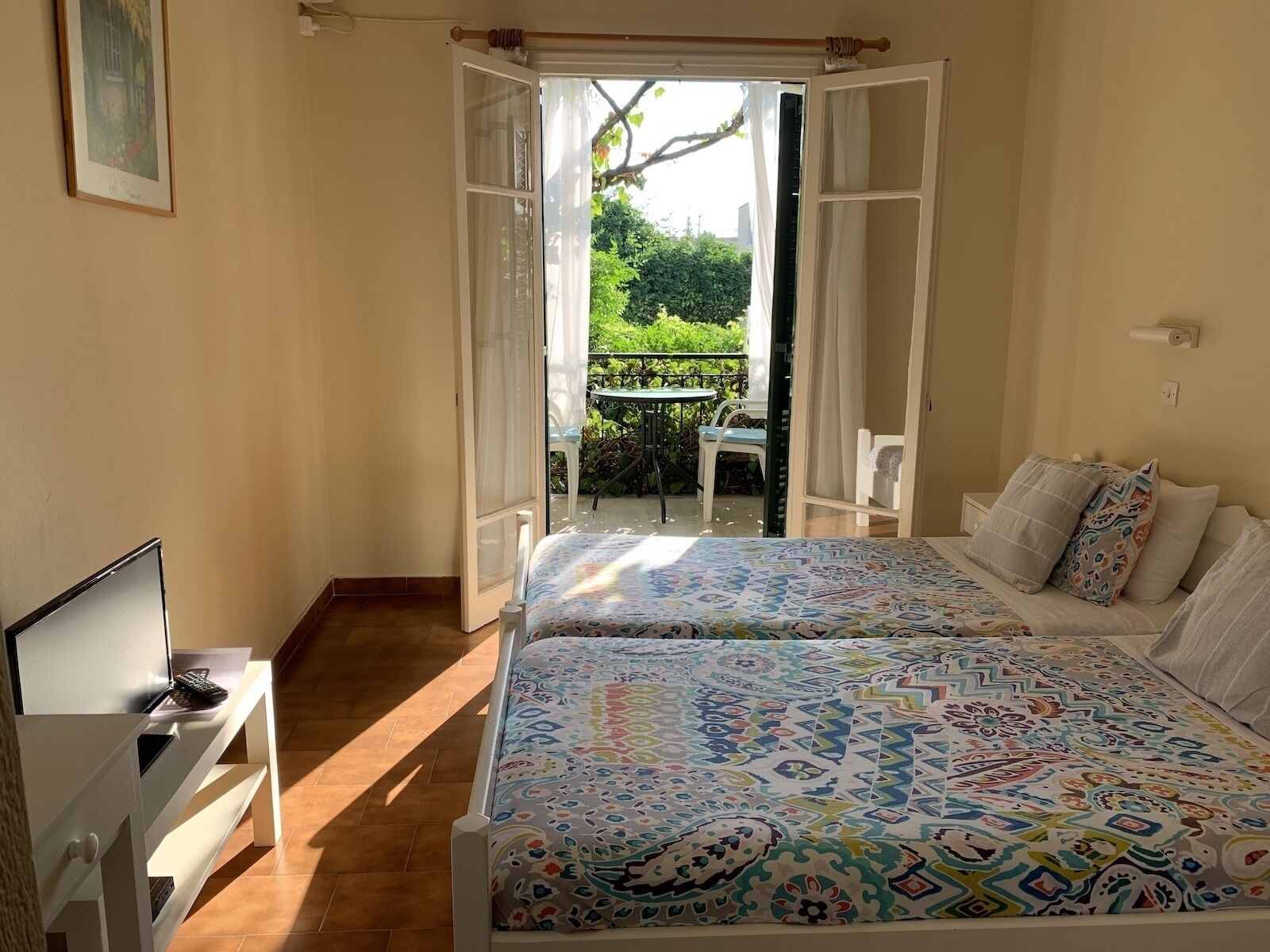 A bedroom with a bed, a TV, a small table, and a balcony with a table and chairs.
