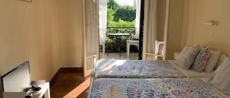 Un dormitorio con cama, televisor, una mesita y balcón con mesa y sillas.