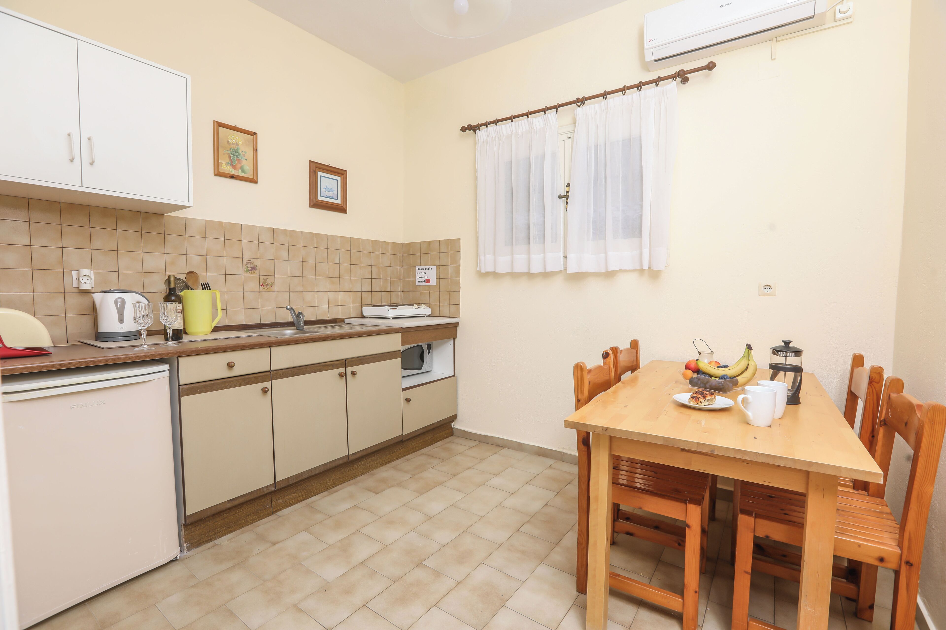Een compacte keuken met een eethoek, inclusief een koelkast, fornuis, spoelbak en een tafel voor twee met stoelen.