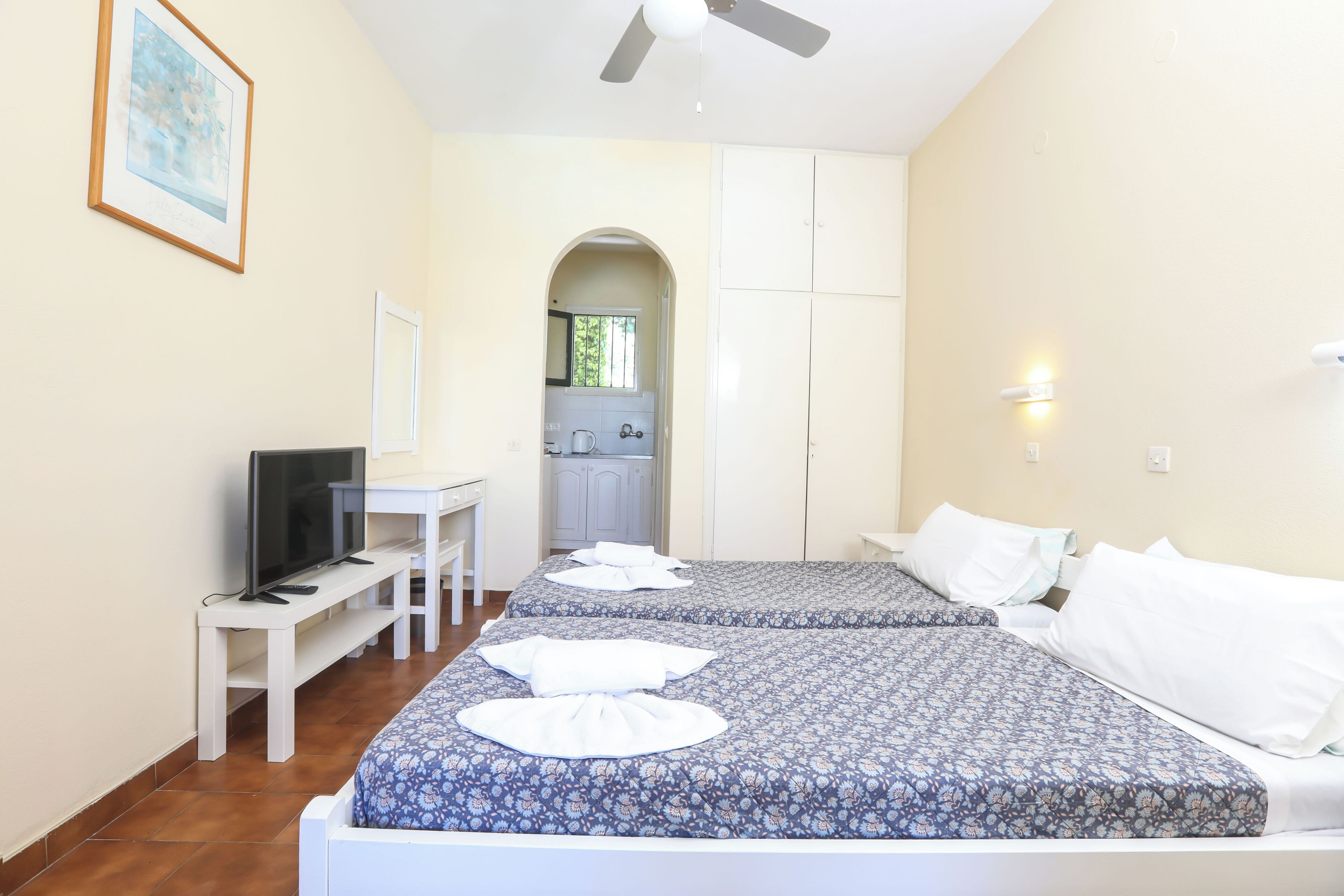 Quarto de hotel com duas camas, televisão, escrivaninha e banheiro visível por um arco.