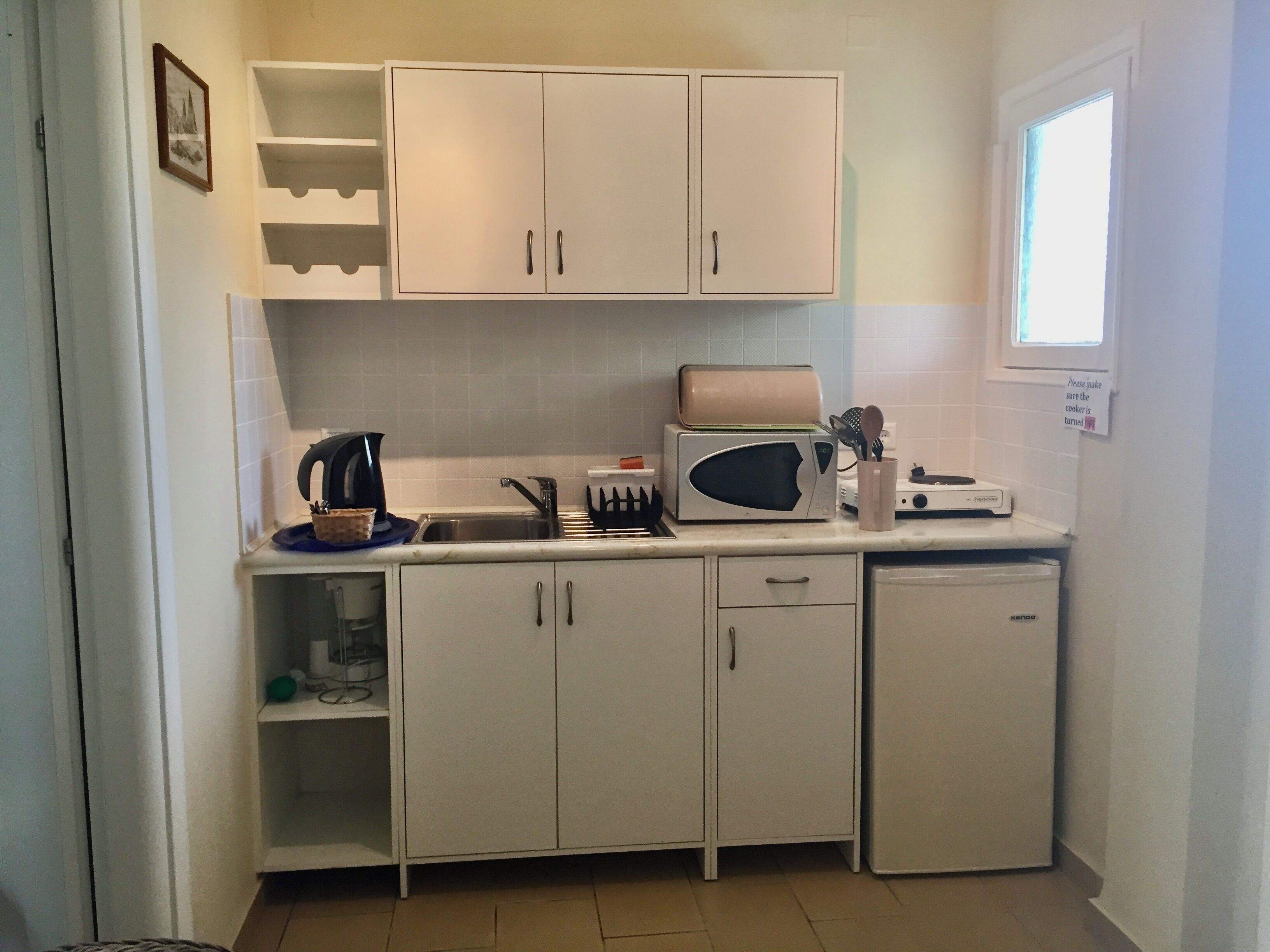 A compact kitchen with white cabinets, a microwave, a kettle, and a toaster.