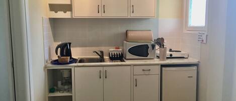 A compact kitchen with white cabinets, a microwave, a kettle, and a toaster.