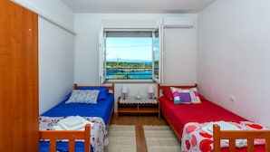 A small, well-lit room with two beds, a window with a view of a body of water and mountains, and a ceiling fan. - Lovely apartment in Kraljevica (Kraljevica)
