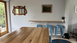A room with a wooden dining table, blue bar stools, a hanging pendant light, a framed mirror, and a painting on the wall. - Ronny's Tootgarook. (Tootgarook)