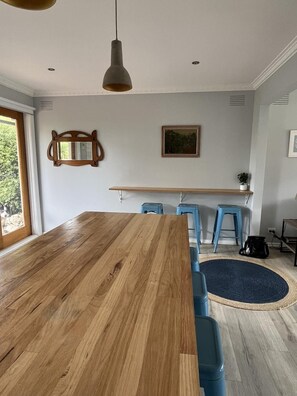 Un coin repas avec une table en bois, des tabourets de bar bleus, une suspension, un miroir et un tableau encadré au mur.