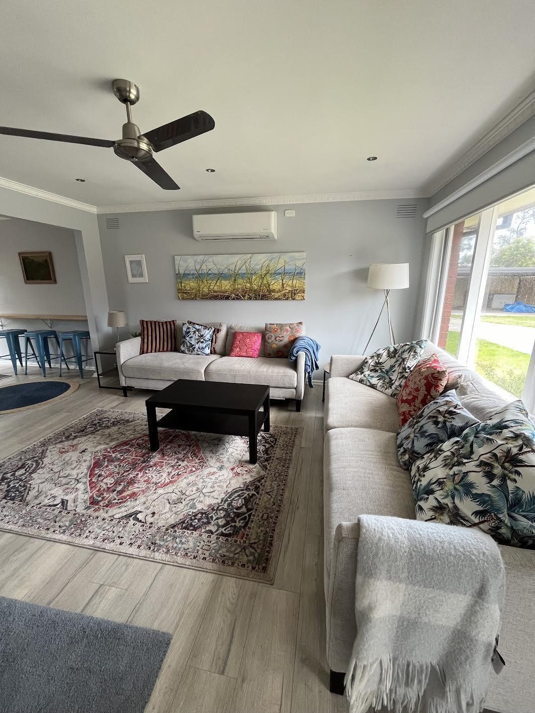 A living room with a ceiling fan, a sofa set, a coffee table, and a large window providing a view of the outdoors.