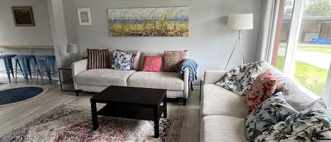 A living room with a ceiling fan, a sofa set, a coffee table, and a large window providing a view of the outdoors.