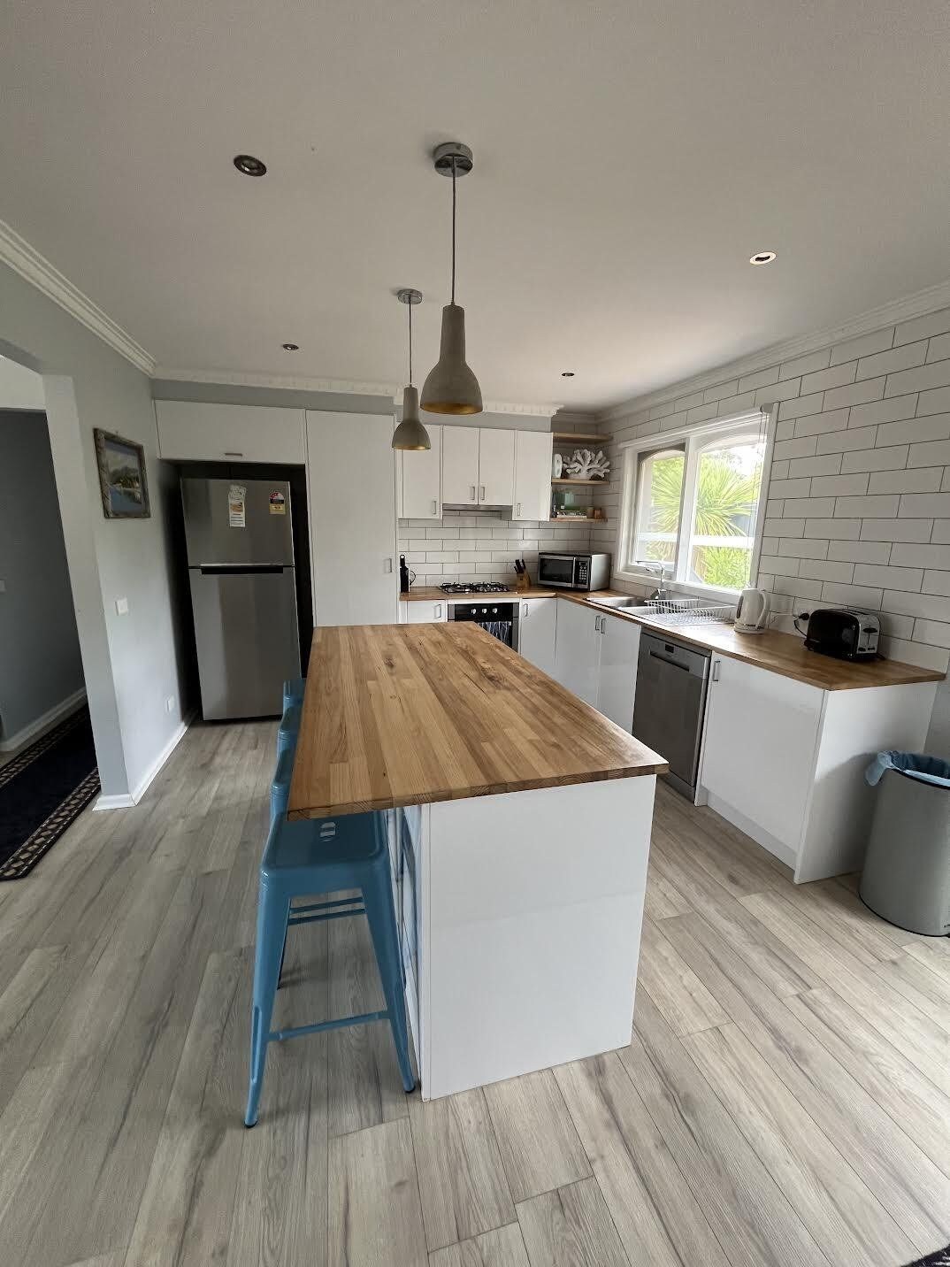 Una cocina moderna con una isla central, armarios blancos y encimera de madera.